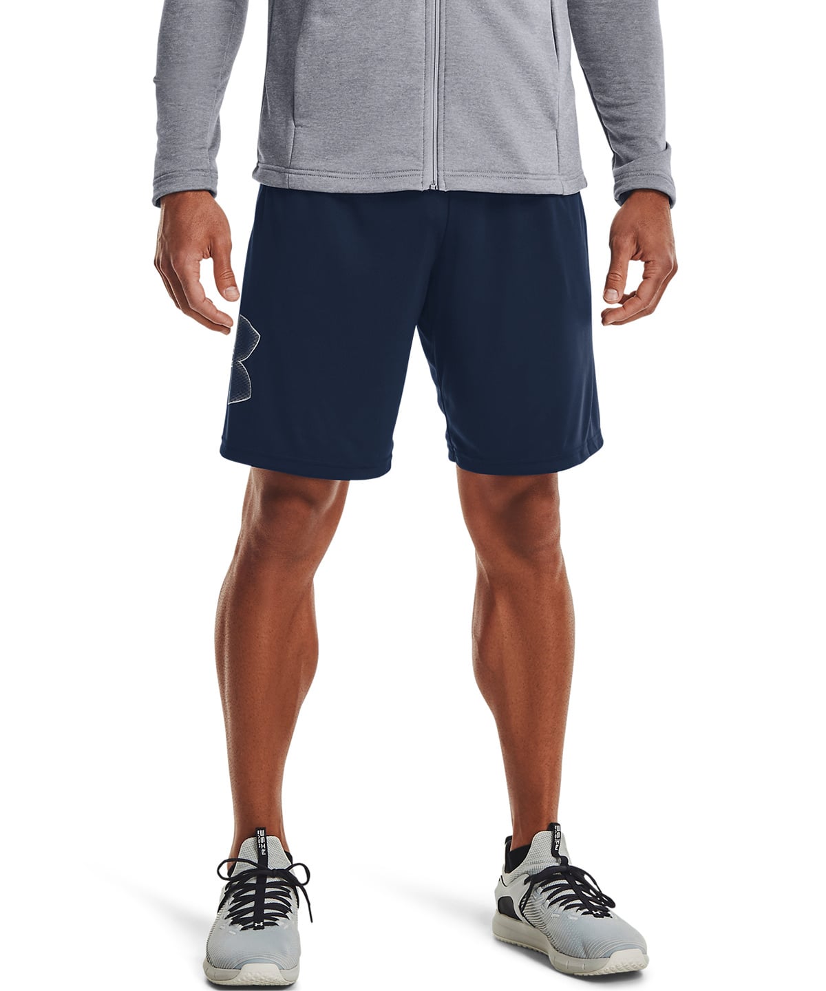 A man wearing navy blue athletic shorts, a gray zip-up hoodie, and gray running shoes, shown from the waist down against a white studio background.