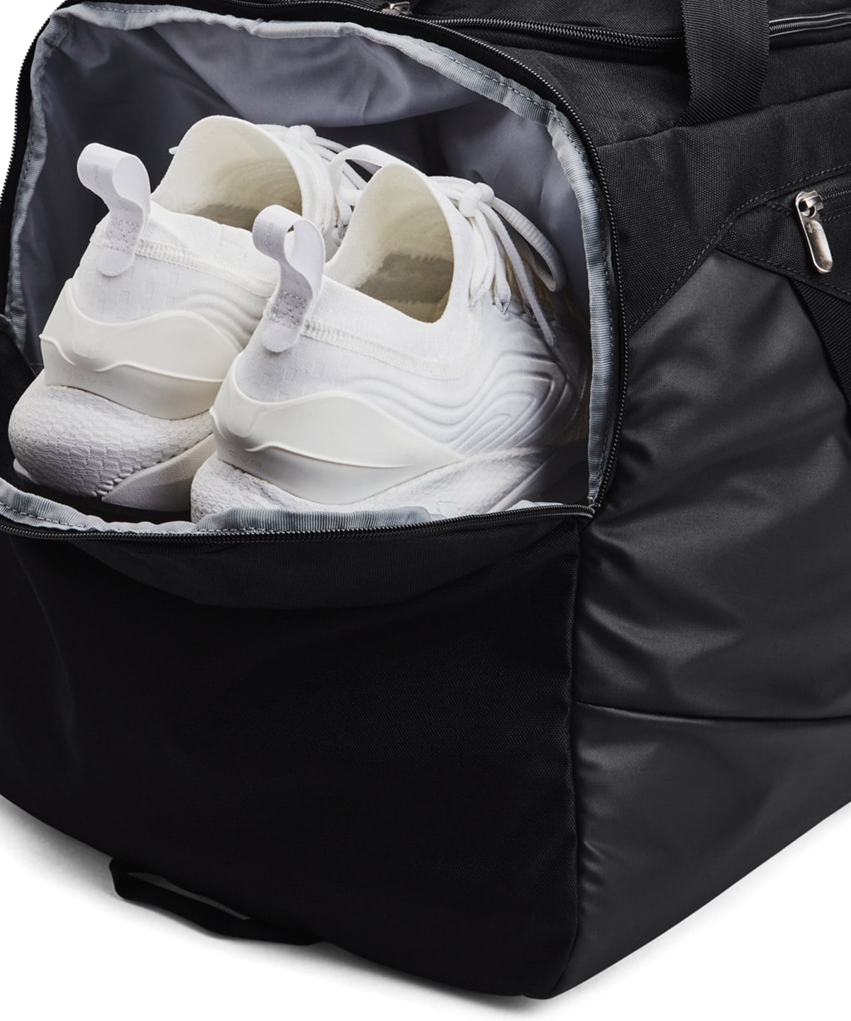 A black duffel bag shown open, containing a pair of white athletic sneakers. The bag has a gray interior lining and a silver zipper pull, photographed on a clean white background.