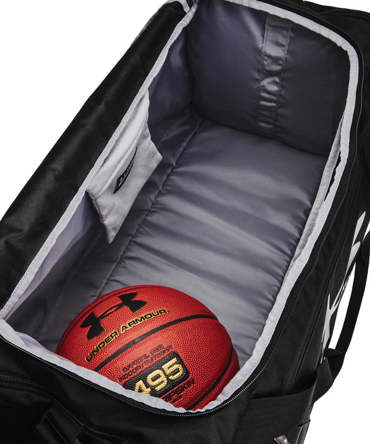 An open black Under Armour duffel bag showing its gray interior lining, with a red Under Armour basketball placed inside.