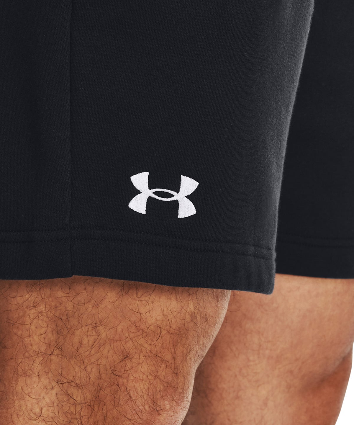 Close-up of black athletic shorts worn by a model, featuring a white Under Armour logo on the left leg and a ribbed hem.