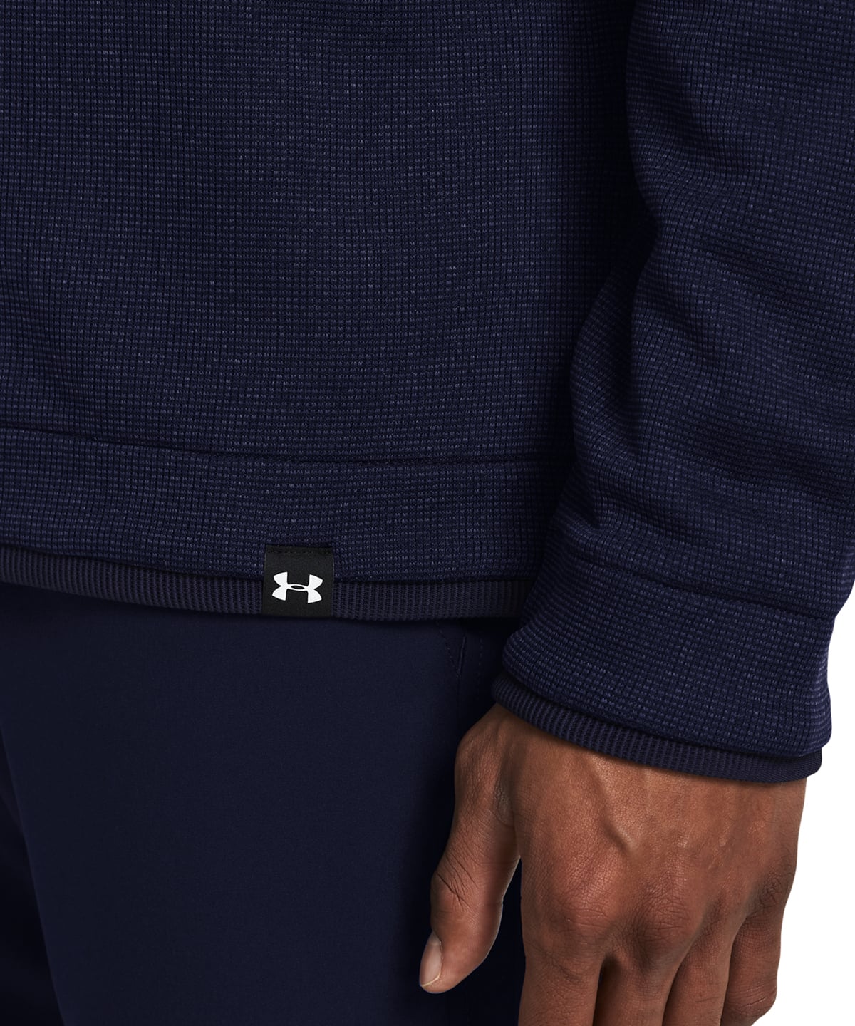 Close-up of a person wearing a dark navy ribbed knit top and matching navy bottoms, with a small Under Armour logo patch at the hem and a hand visible at the wrist.