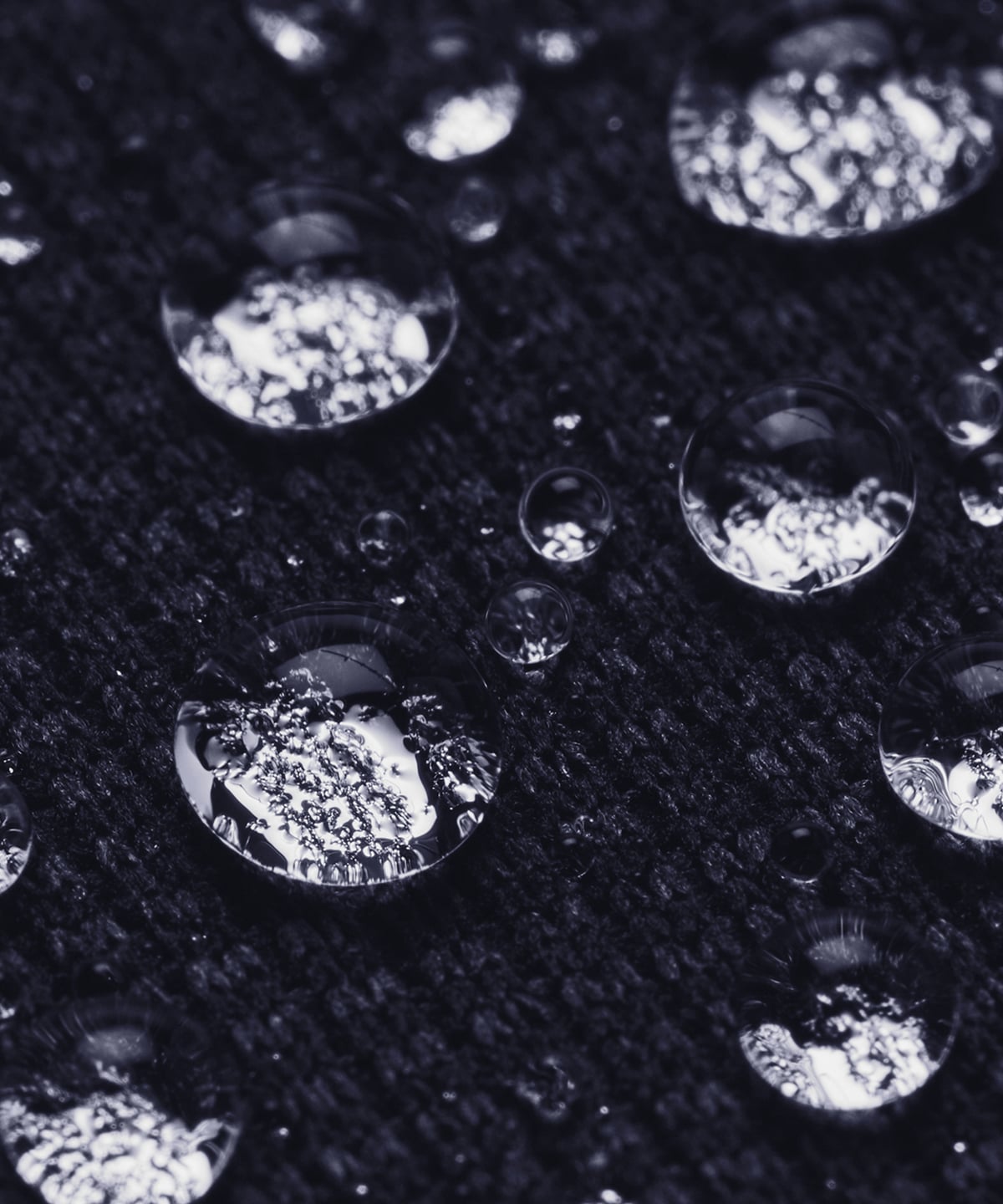 Close-up of clear water droplets resting on a dark textured fabric surface.